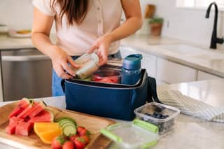 Padre preparando una bolsa térmica con snacks saludables y agua para un niño pequeño en verano