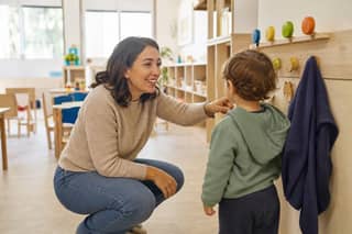 Educadora de guardería presenta a un peque su nuevo perchero y la estantería de juegos en el aula