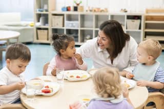 Niños comiendo en el comedor de una guardería con supervisión de una educadora