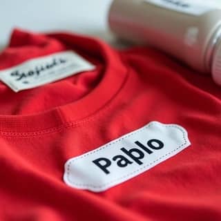 Primer plano de diferentes etiquetas personalizadas (termoadhesivas, adhesivas, de coser) en una variedad de objetos infantiles como ropa, botella y estuche.