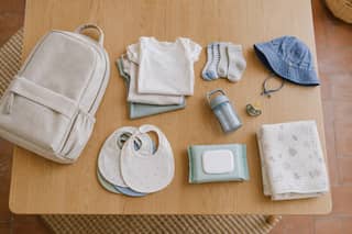 Contenido organizado de una mochila de guardería: ropa de repuesto, biberón, toallitas y manta