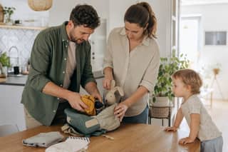 Padres preparando la mochila de un niño con ropa de recambio y un objeto de apego antes del primer día en la guardería