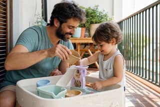 Padre y niño pequeño jugando con agua en terraza sombreada en verano