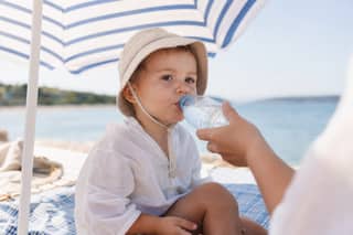 Niño pequeño bebiendo agua a la sombra tras bañarse en verano