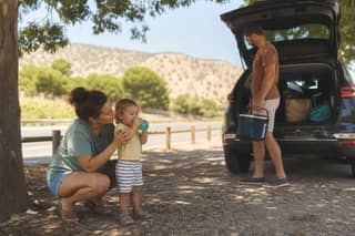 Familia haciendo una parada en ruta con un niño pequeño para estirar piernas y beber agua