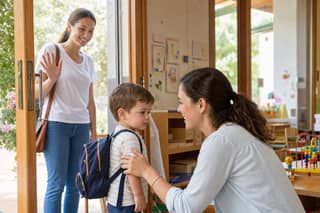 Educadora recibiendo con calma a un niño pequeño en la puerta de la guardería mientras la madre se despide sonriendo
